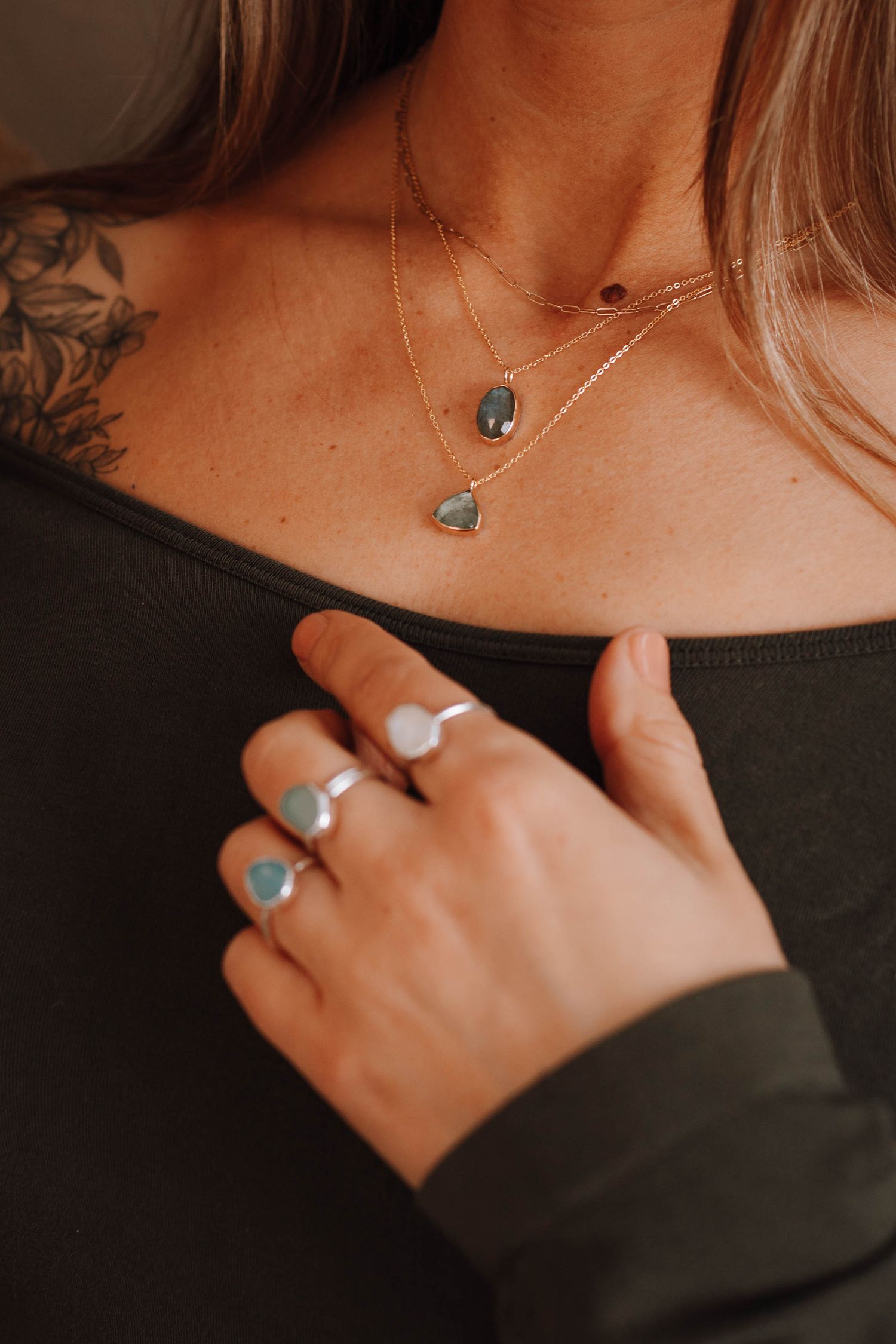 Multiple turquoise stone rings and layered necklaces styled with dark clothing.