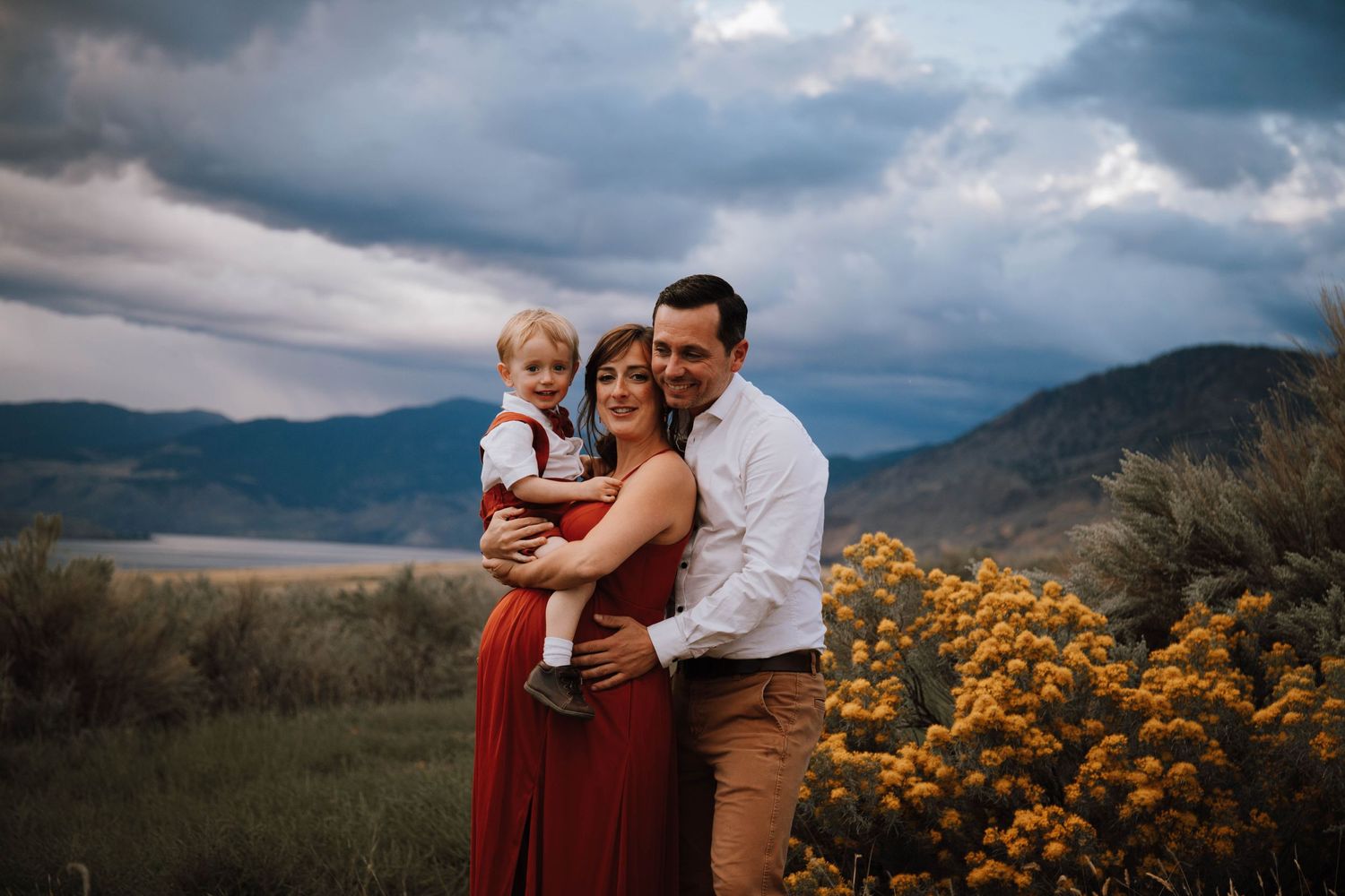 Family standing together against dramatic mountain backdrop with blooming yellow wildflowers.