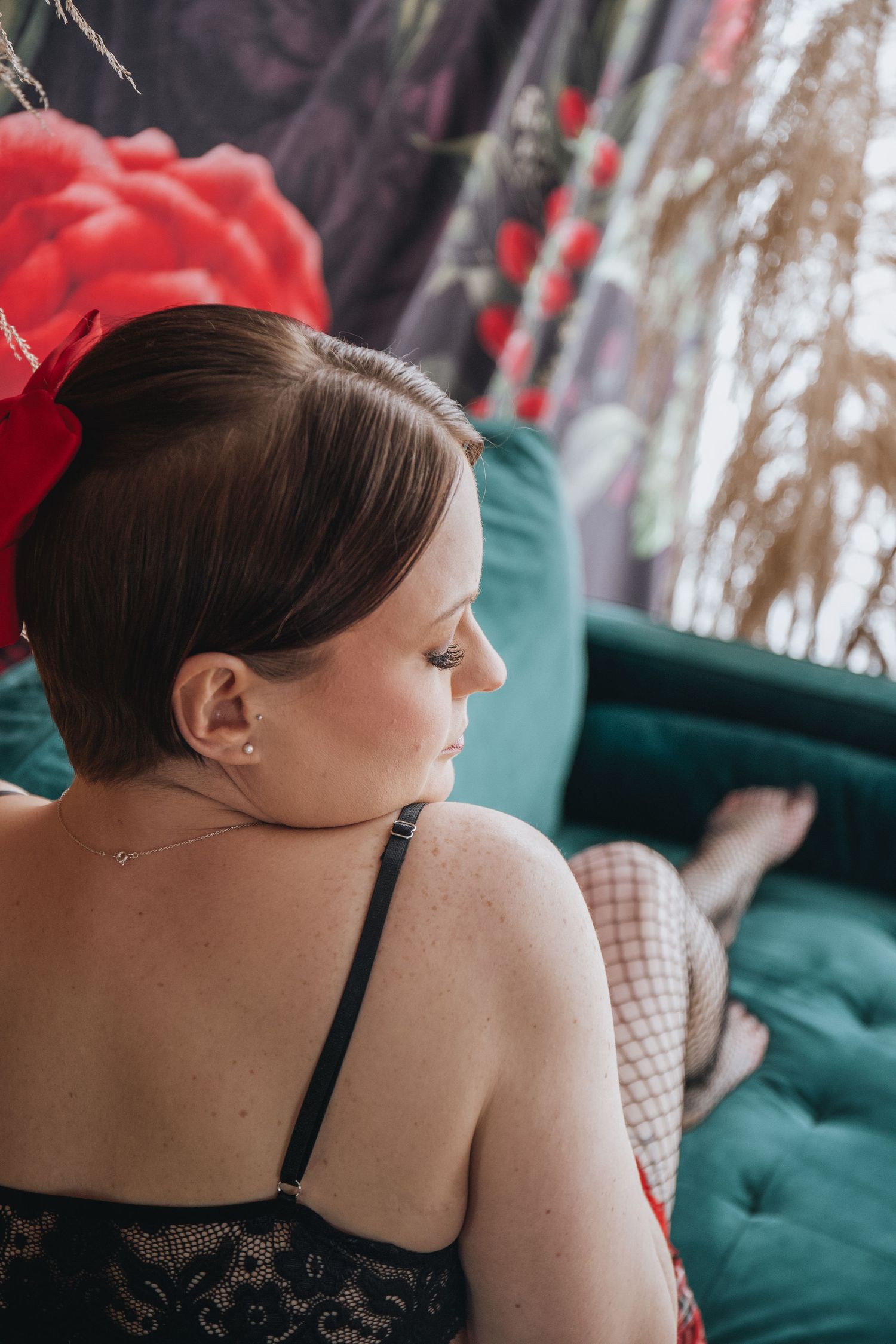 Artistic boudoir portrait with red hair accessory against emerald tufted couch.