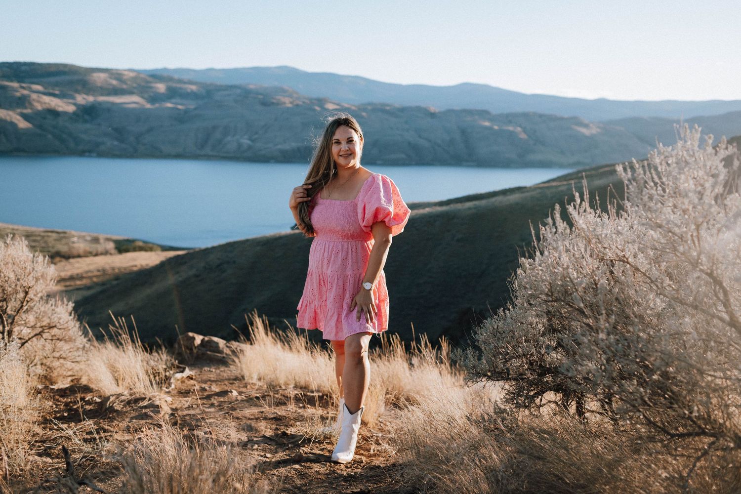 A pink dress stands out against a scenic mountain lake backdrop on a clear day.