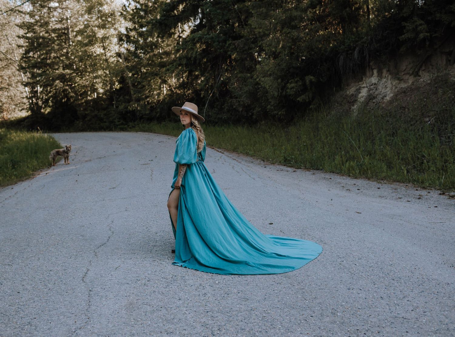 Turquoise dress with long train flows elegantly on forest path.