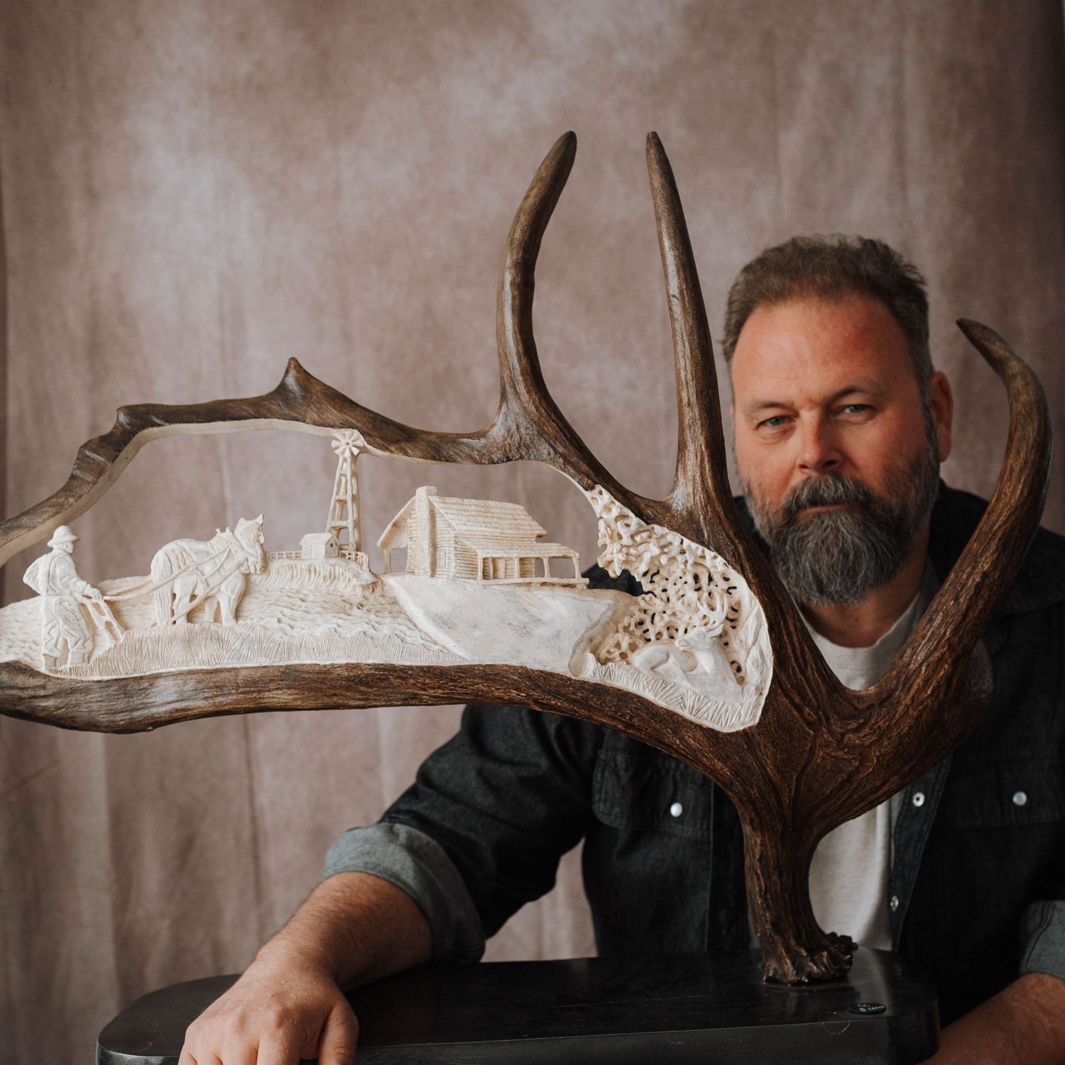 An artist displays intricate carved artwork on antlers featuring miniature wildlife scenes.