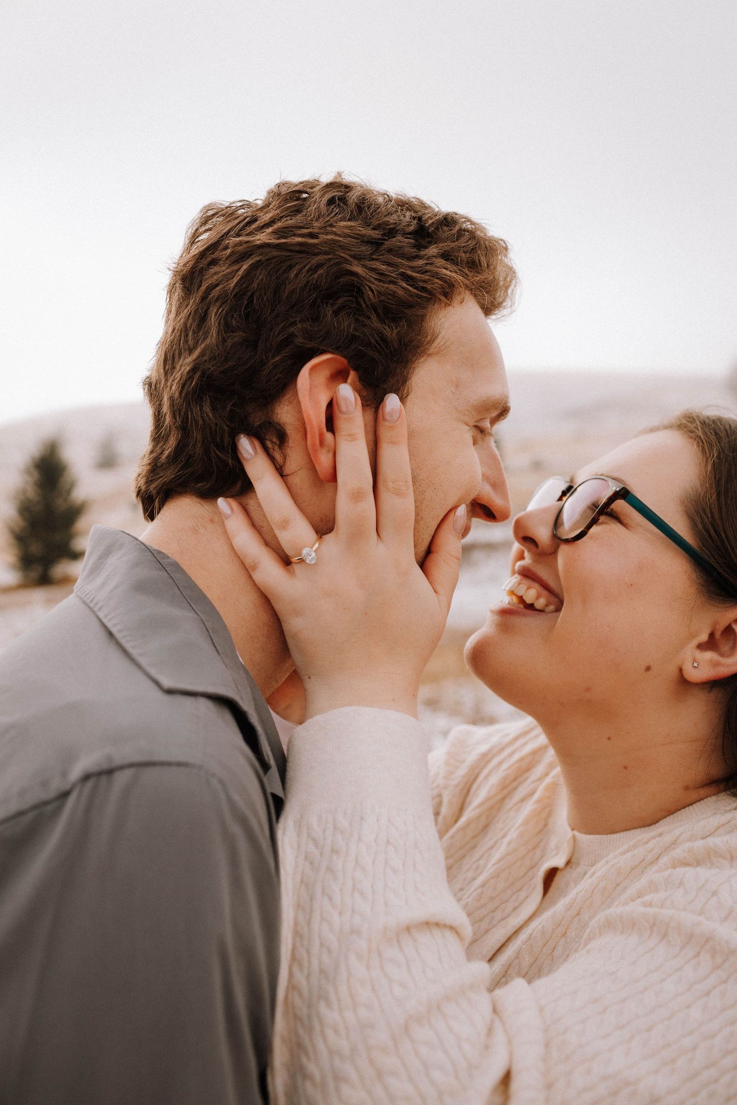 A romantic outdoor portrait of a couple sharing an intimate moment while wearing casual sweaters in nature.