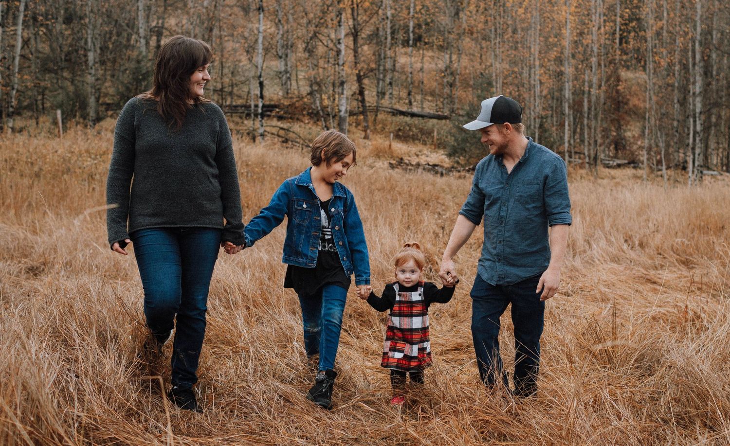 A family walks together through tall golden grass in an autumn field.