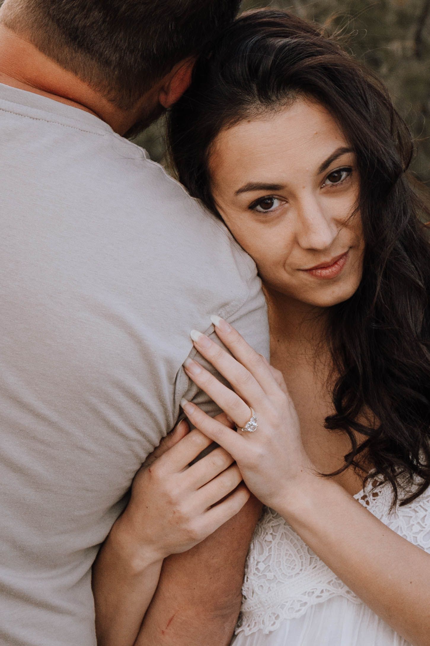 A close-up engagement photo shows a couple embracing while she shows her ring and smiles at the camera.