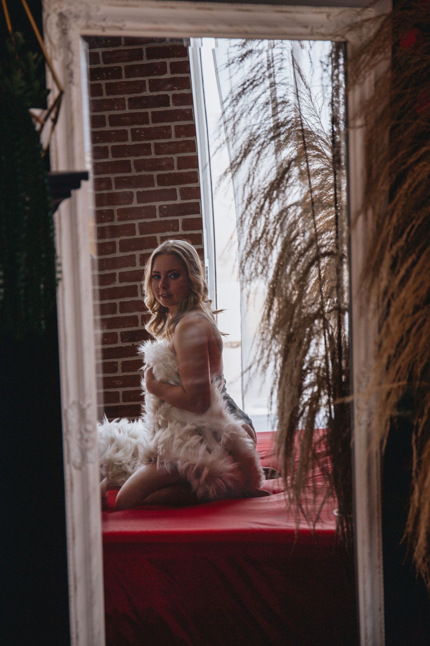 Artistic mirror reflection portrait with dried pampas grass and brick wall decor.