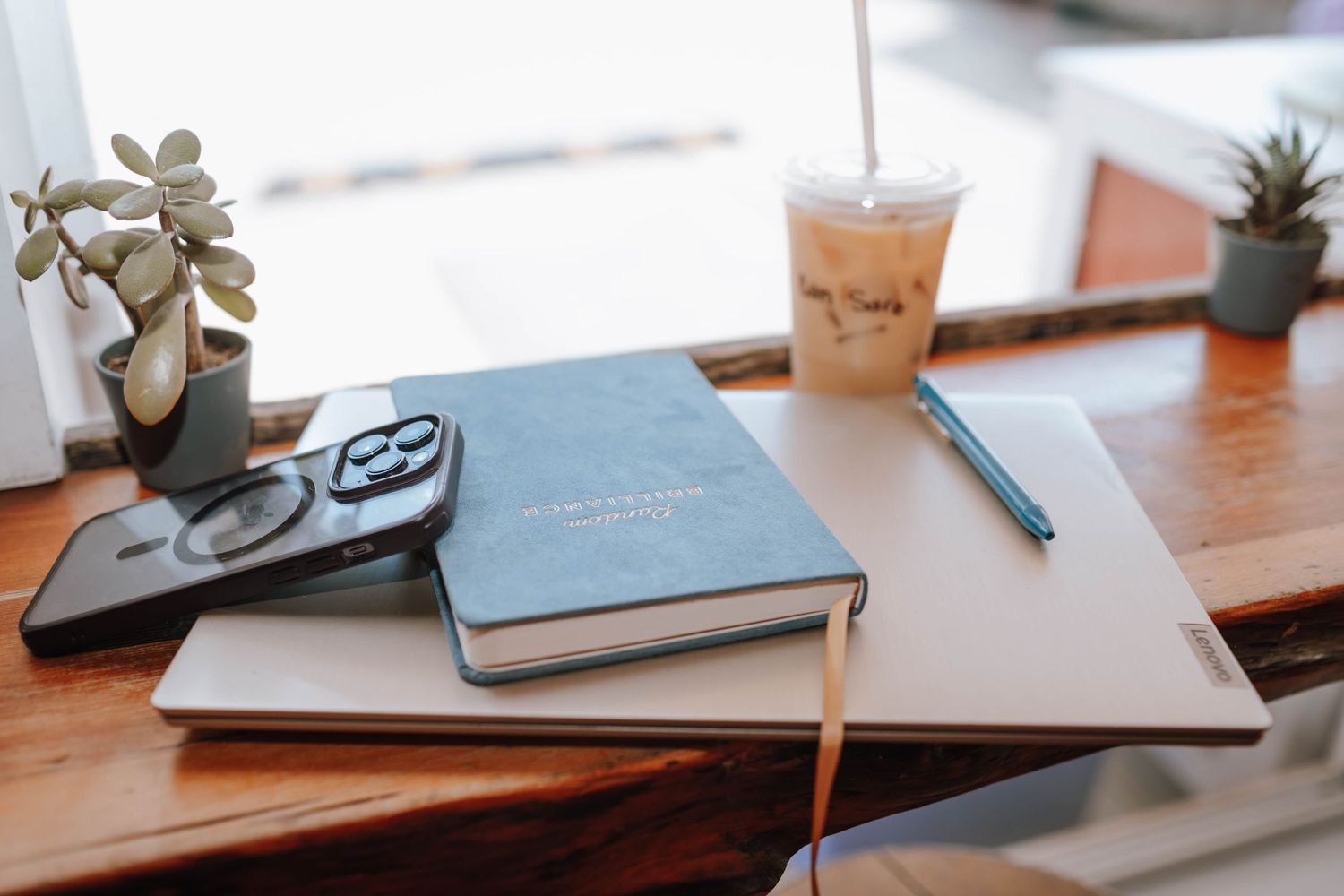 Workspace arrangement with notebooks, glasses, and an iced coffee on a wooden table.