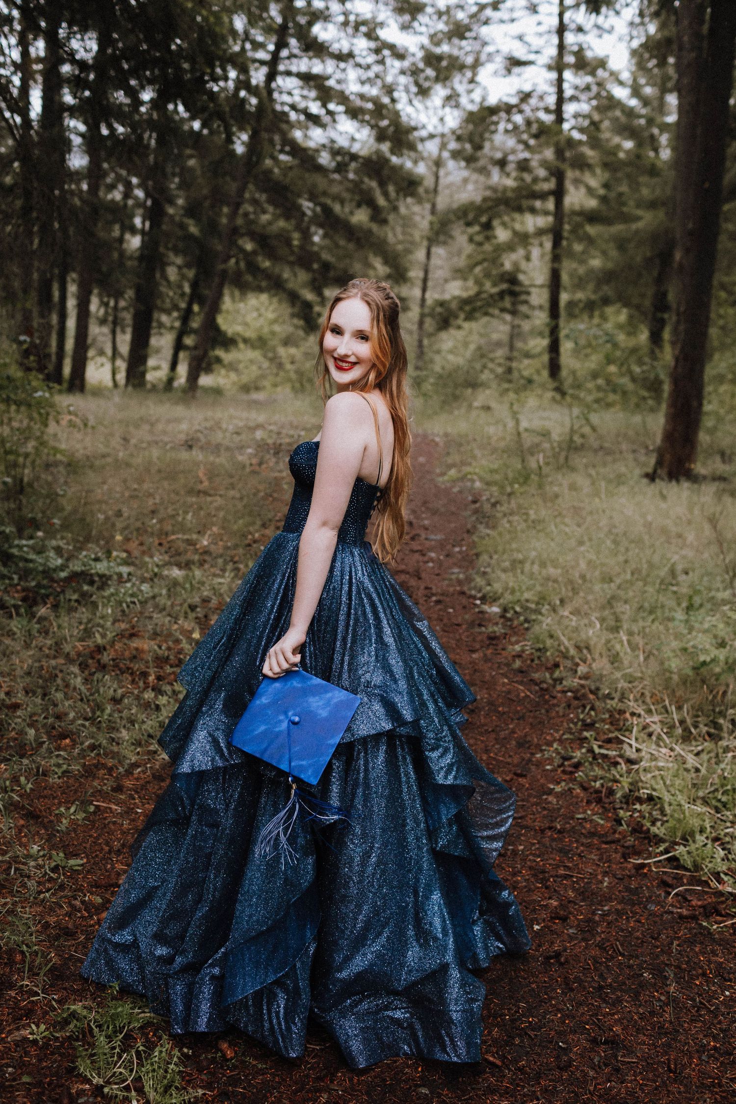 A navy blue ballgown sparkles as its wearer twirls on a forest path.