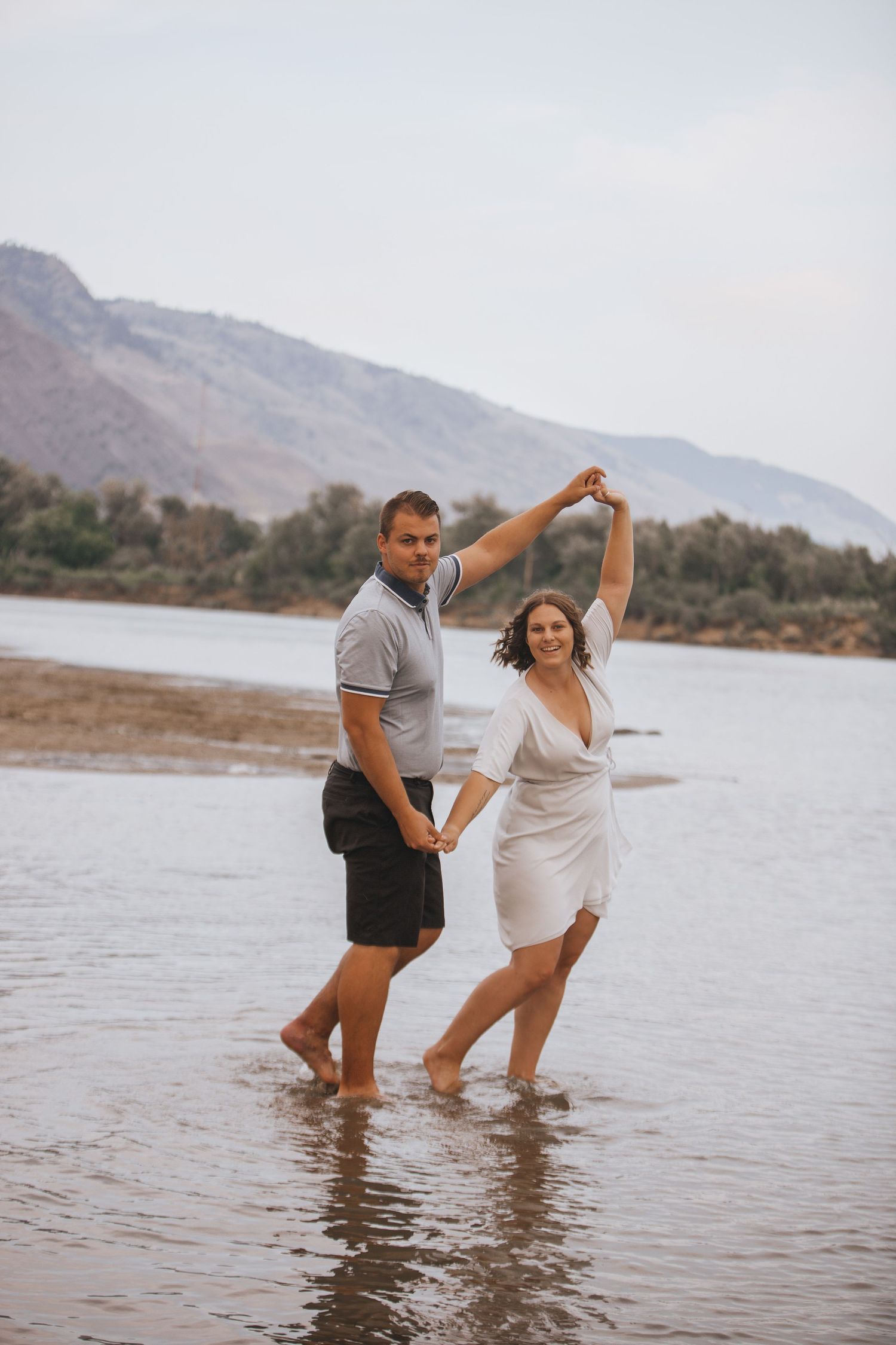 Dancing together in a lake with mountains and trees in the distance.