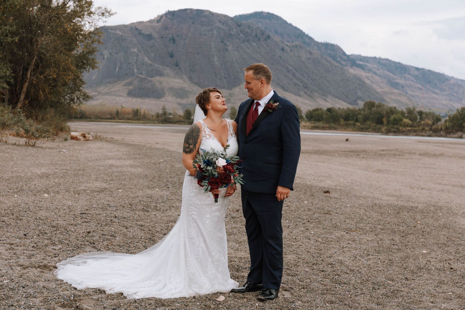 A couple shares a candid moment in their wedding attire against a mountainous desert backdrop.
