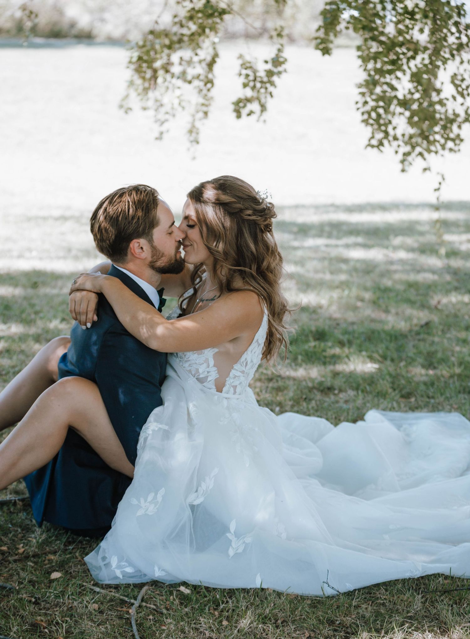 Romantic moment captured under tree branches with bride in elegant lace gown.