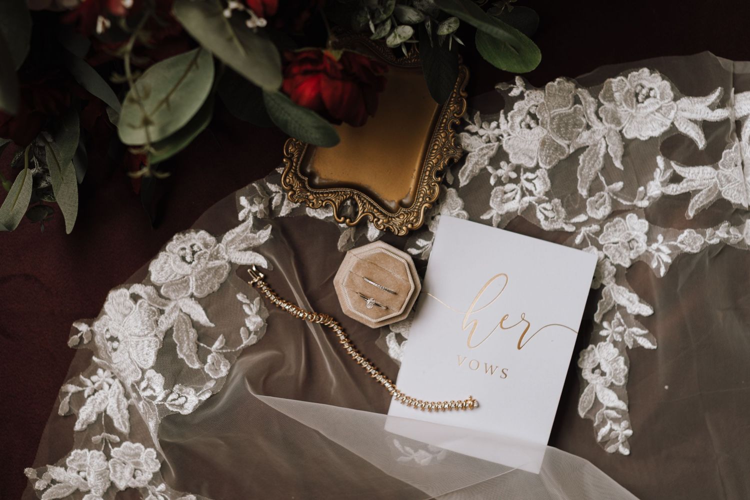 Elegant wedding flat lay with lace veil, gold hexagon box, pearl bracelet, and calligraphy card on dark surface.