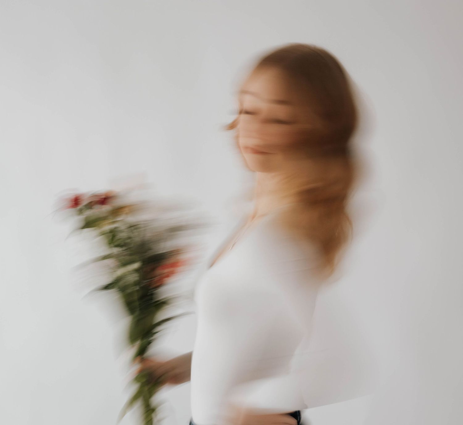 Artistic motion blur portrait with white dress and flowers against light background.