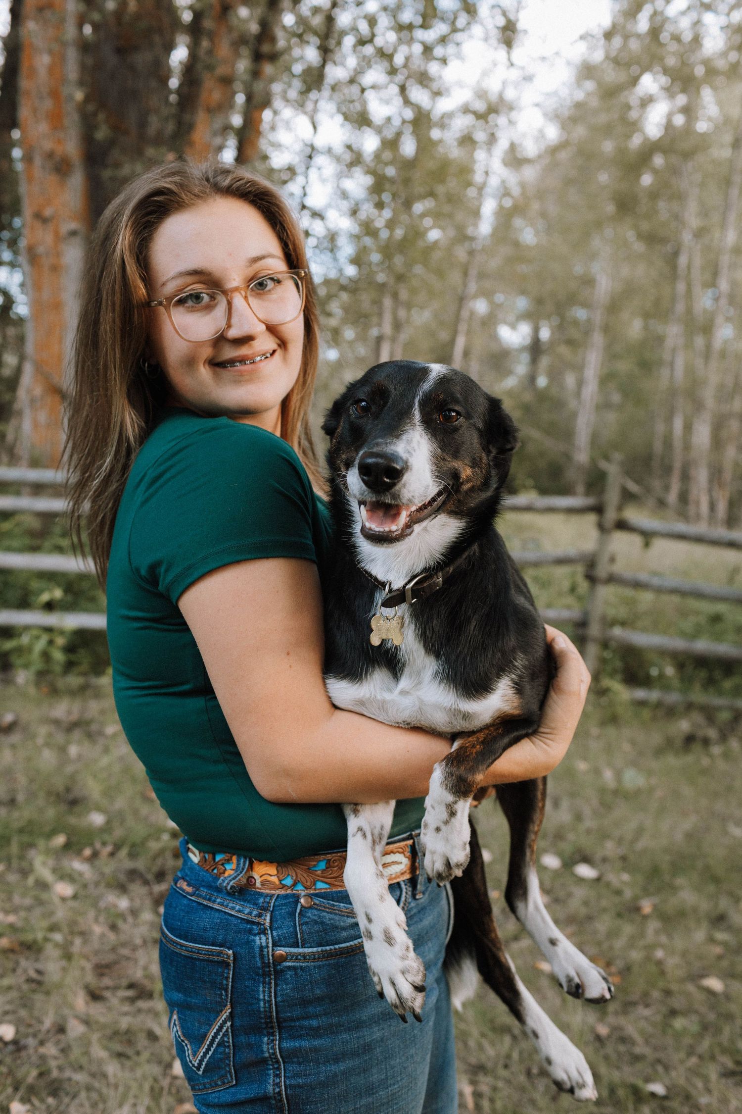 A Border Collie mix with black and white fur is held and hugged outdoors against a backdrop of autumn trees.