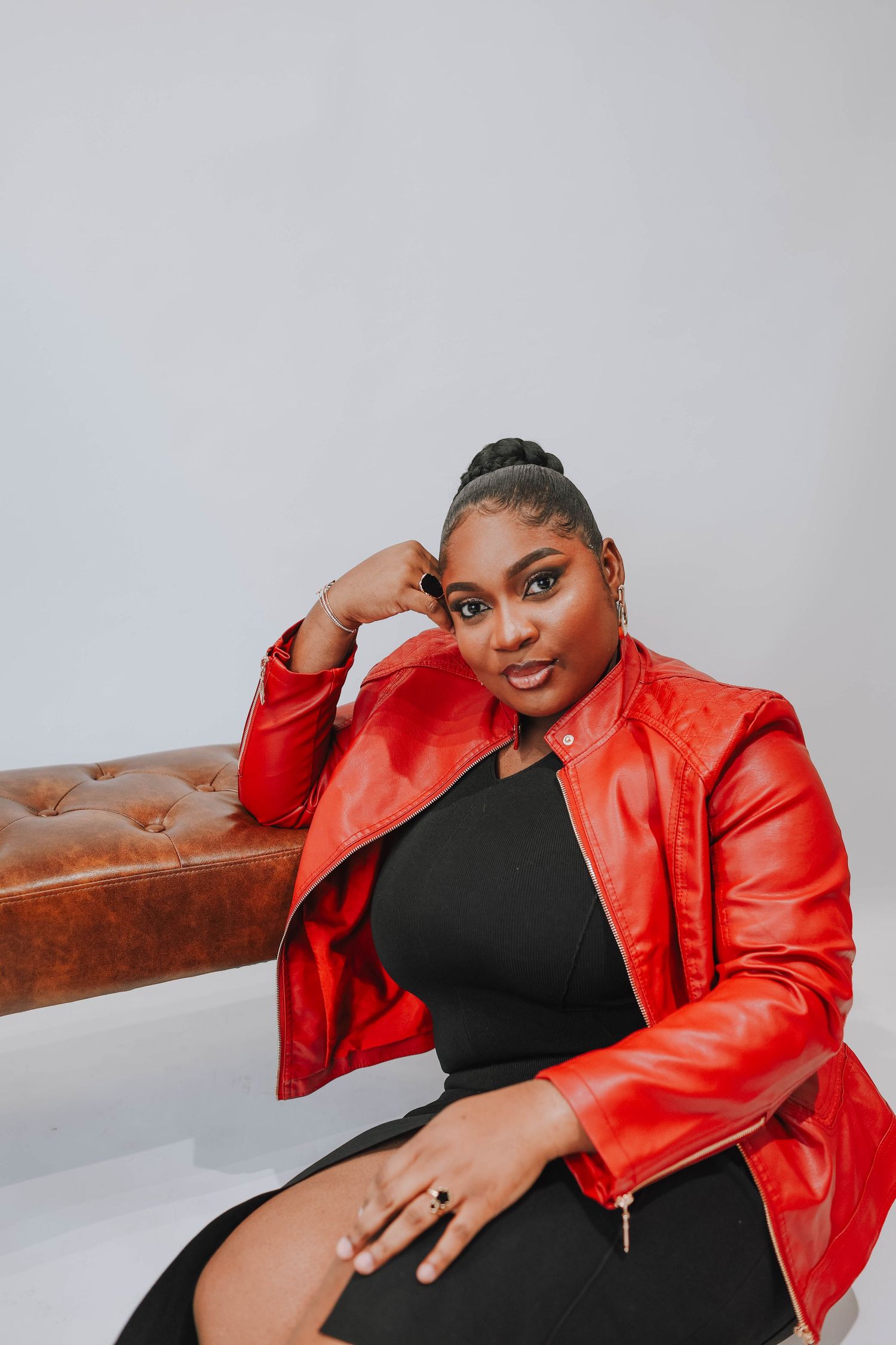 Plus size model in vibrant red leather jacket and black dress poses confidently against neutral background.