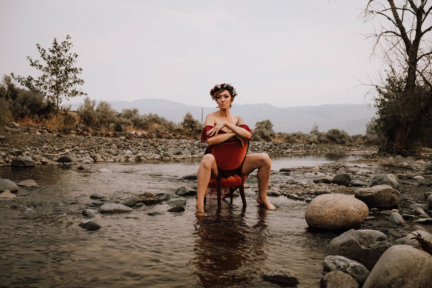 Moody portrait session with antique chair positioned among river rocks and mountains.