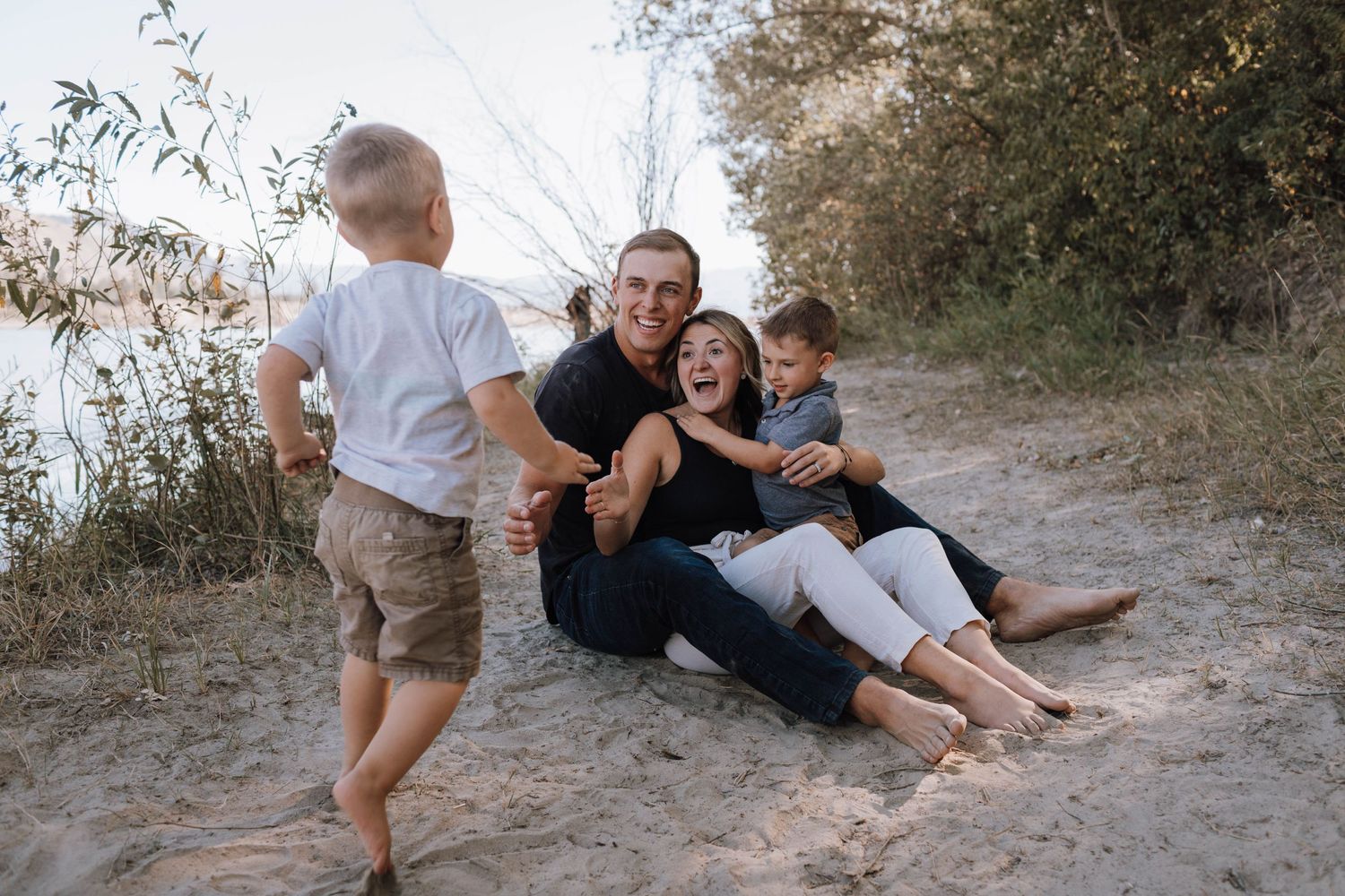 A joyful family laughs together while relaxing outdoors on a sandy beach path during a casual photoshoot.