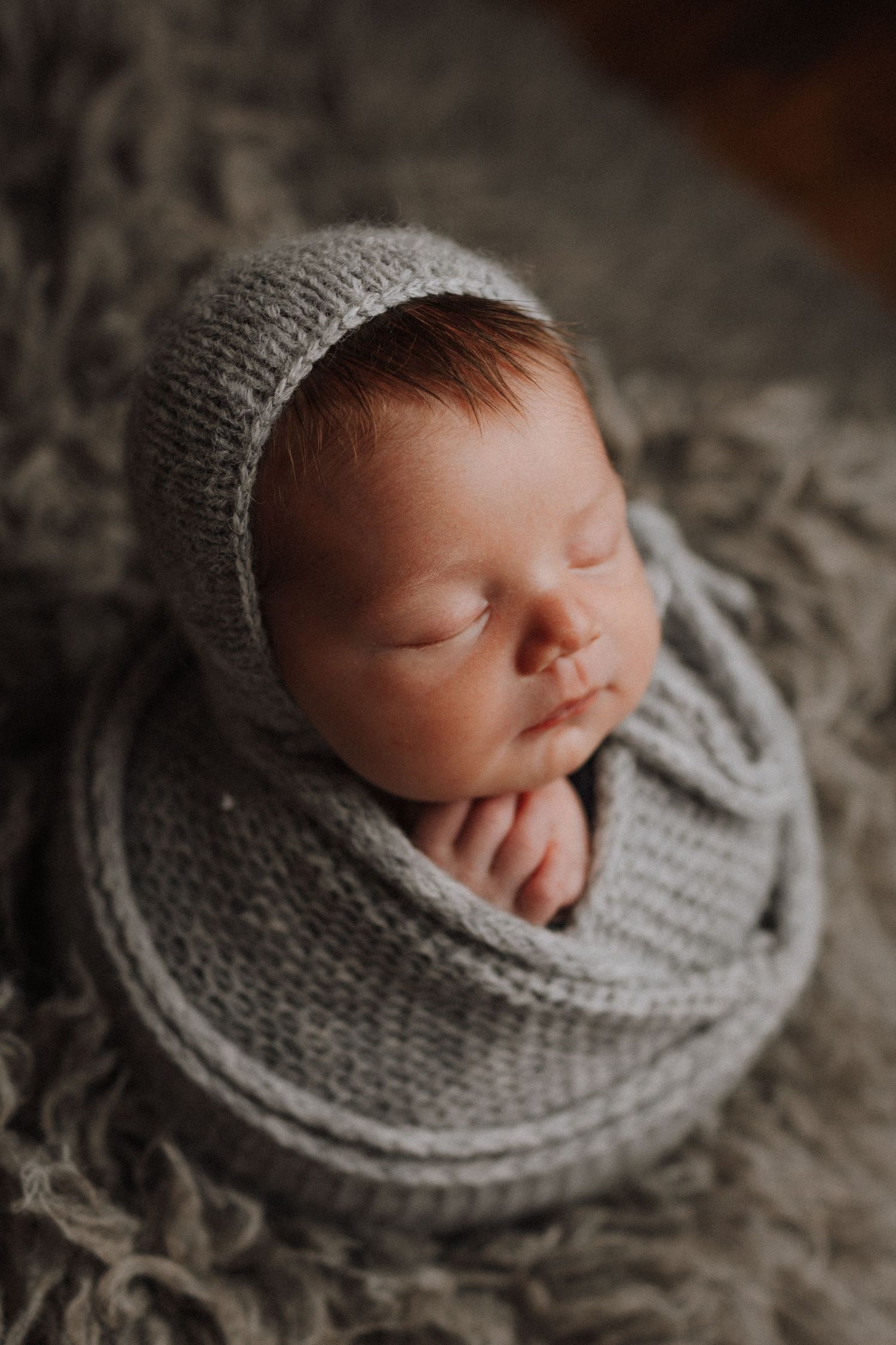 Sleeping newborn wrapped in soft gray knit blanket shown from different angles in artistic black and white photography.