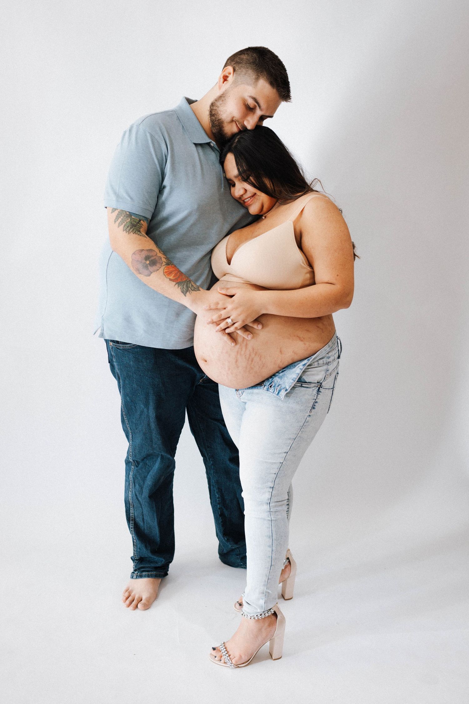 Intimate maternity photo of couple embracing against white backdrop, showing affectionate connection.