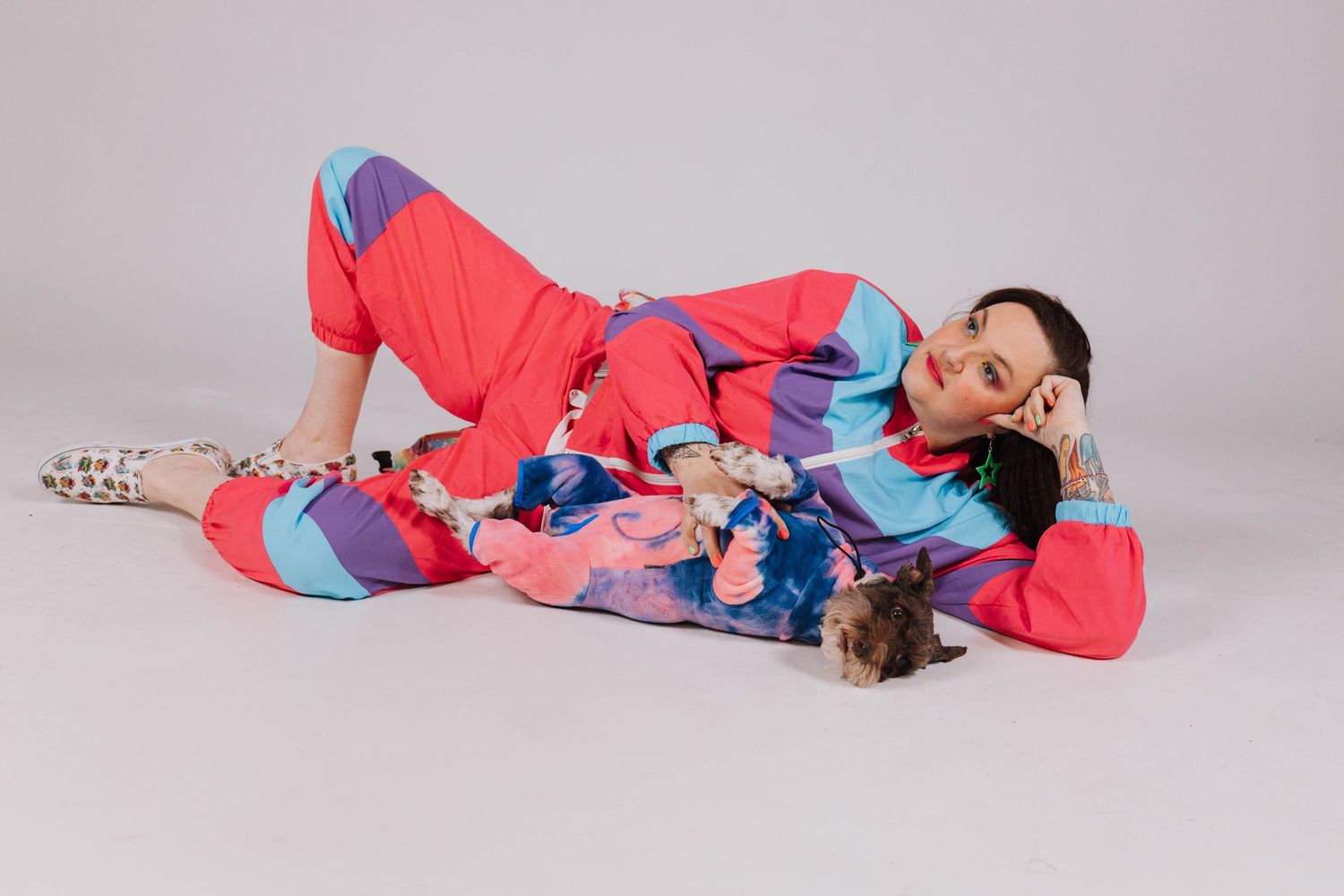 A person wearing colorful pastel blue and coral loungewear lies on the ground in a playful pose against a light background.