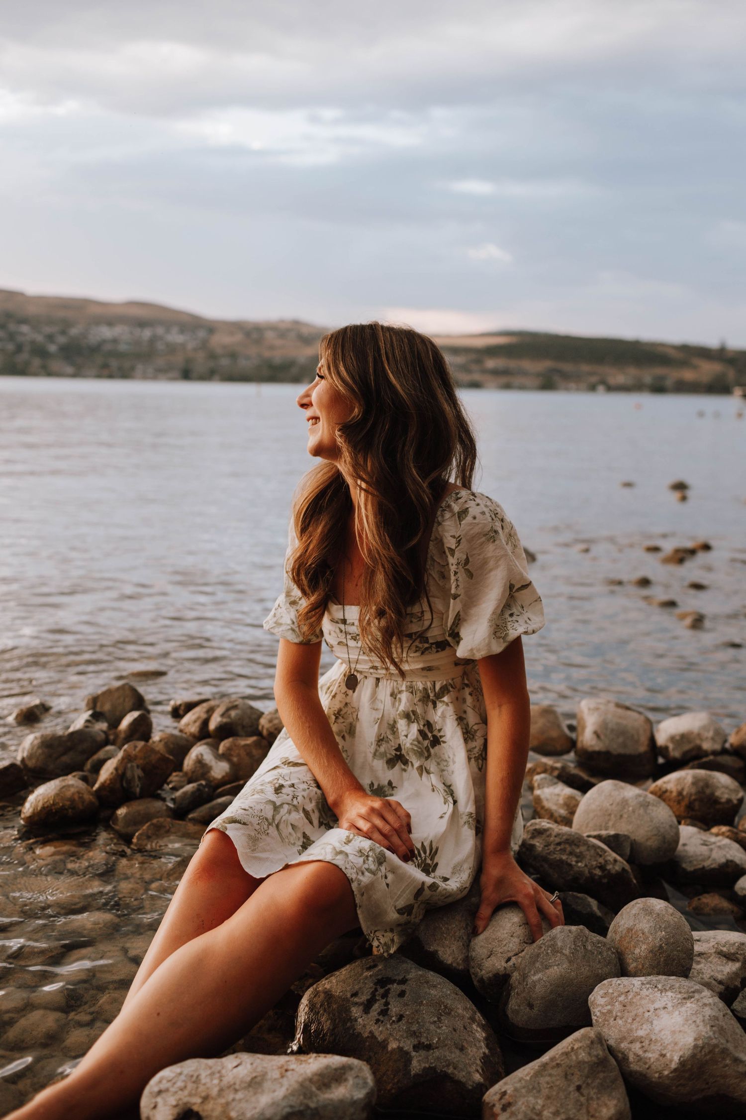 White dress contrasts against rocky shoreline as waves lap at the lake's edge.