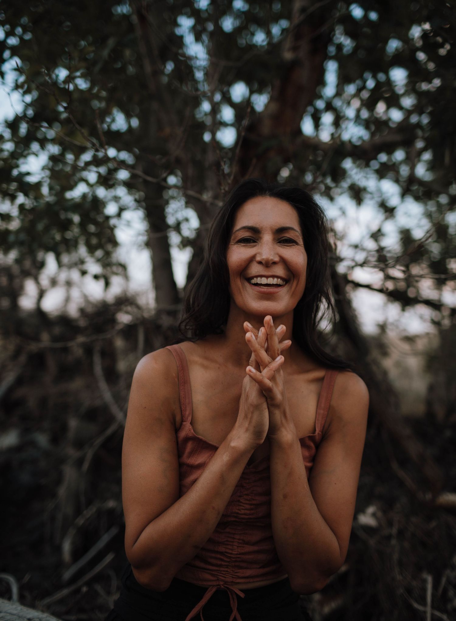 A joyful outdoor portrait taken under tree branches at dusk.