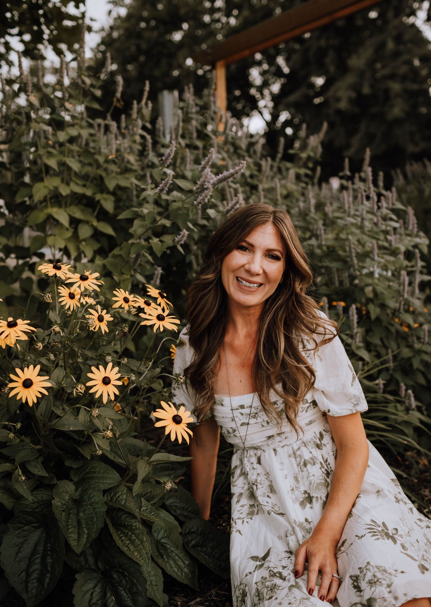 A white floral dress contrasts beautifully against vibrant yellow daisies in a lush garden setting.