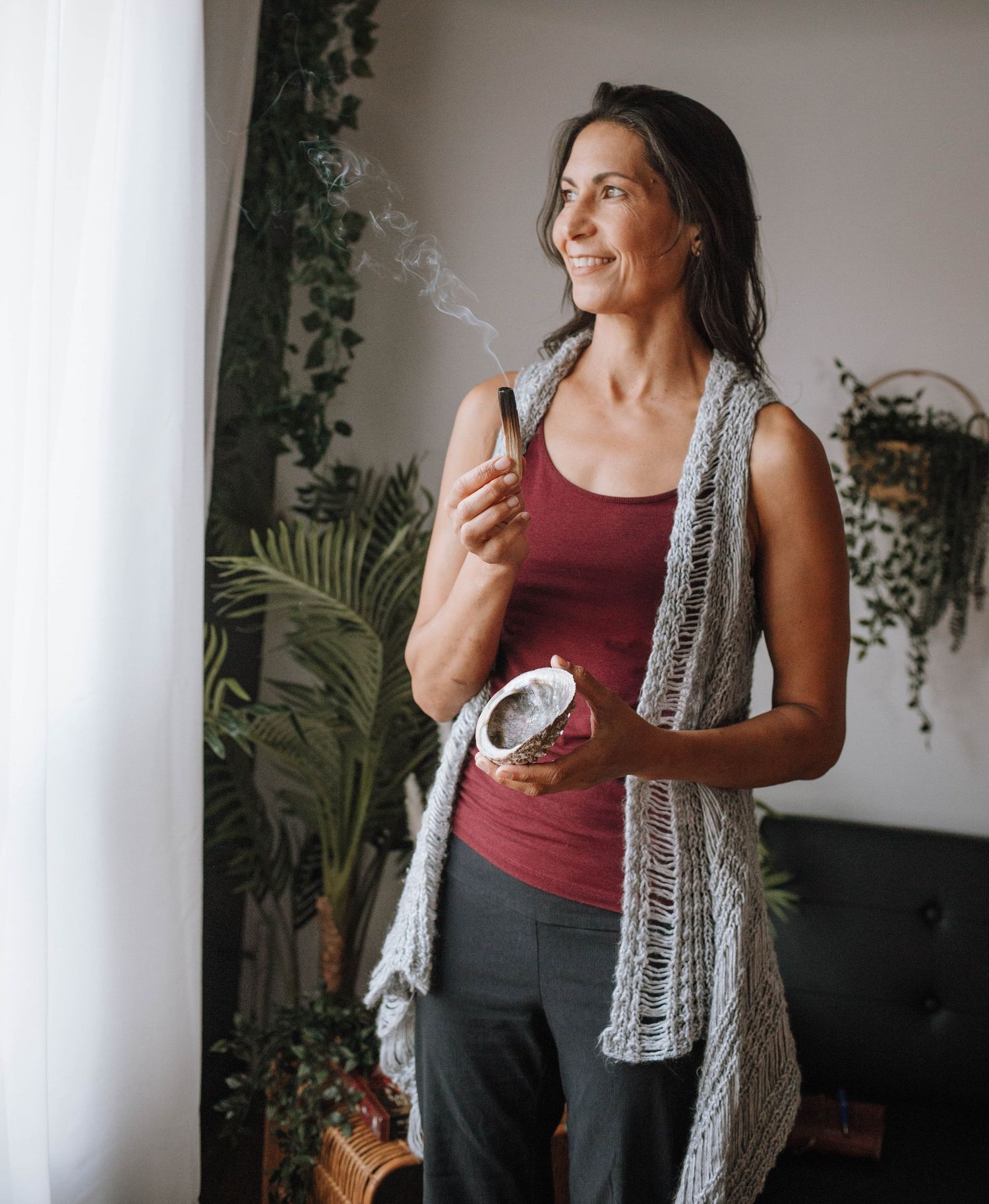 An indoor scene with plants showing someone wearing a red tank top and knit cardigan.