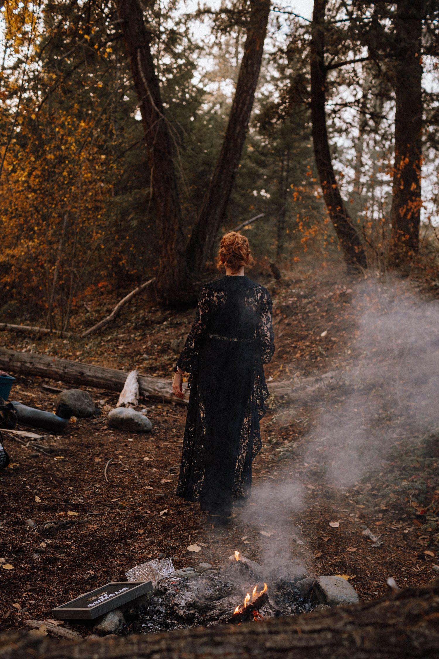 A row of small fires burning in a dark wooded area with black signs placed between them.