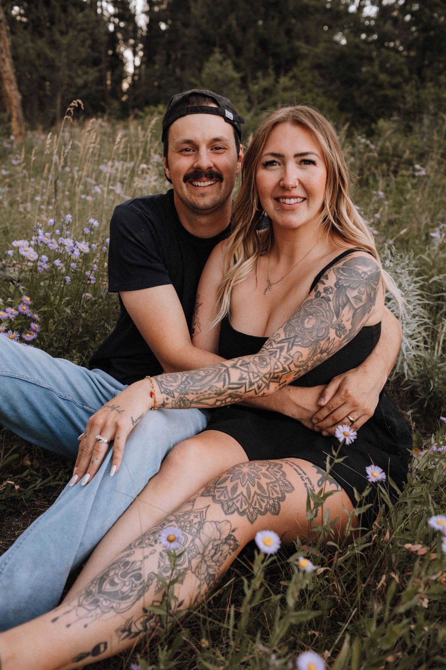 A couple sits together in a wildflower meadow during a romantic outdoor photo session at sunset.