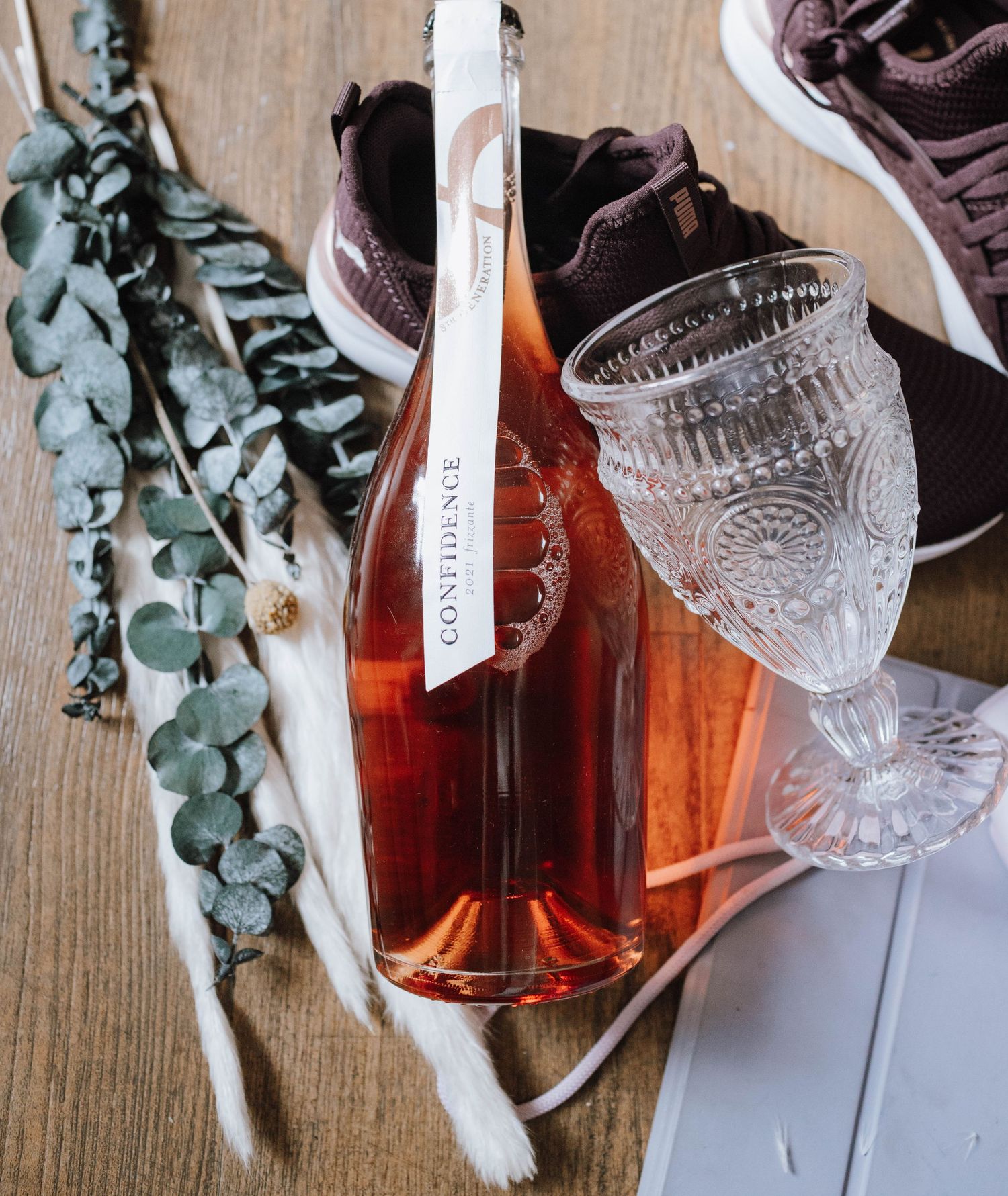 Rose wine bottle with crystal glasses and eucalyptus branches on wooden surface.