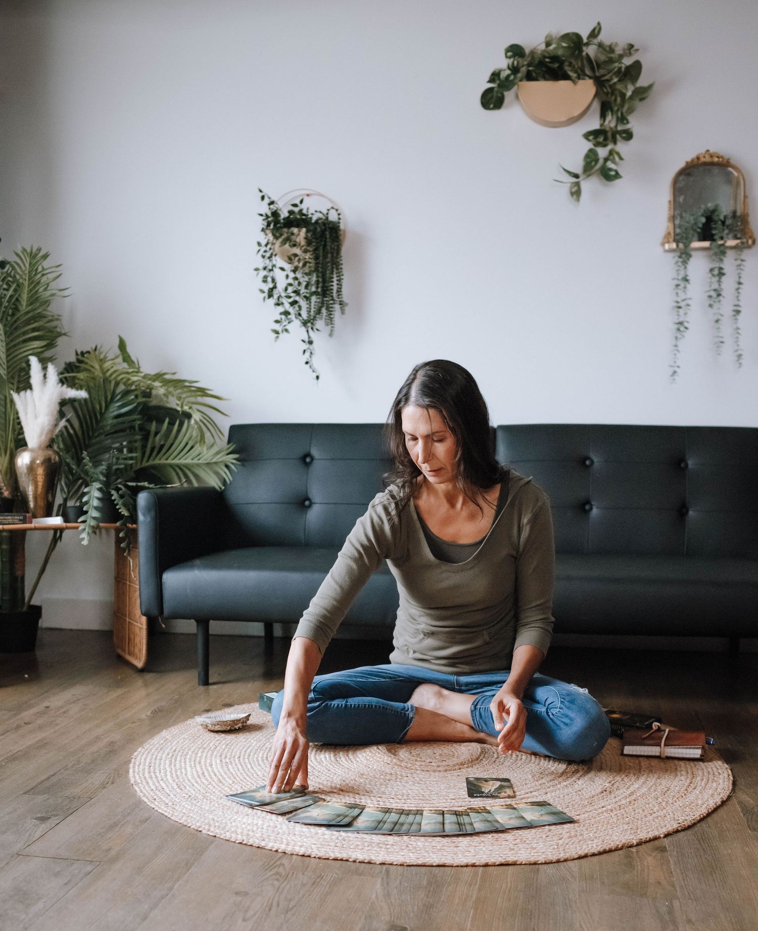 A cozy living room setting with trailing plants and someone seated on a round jute rug.