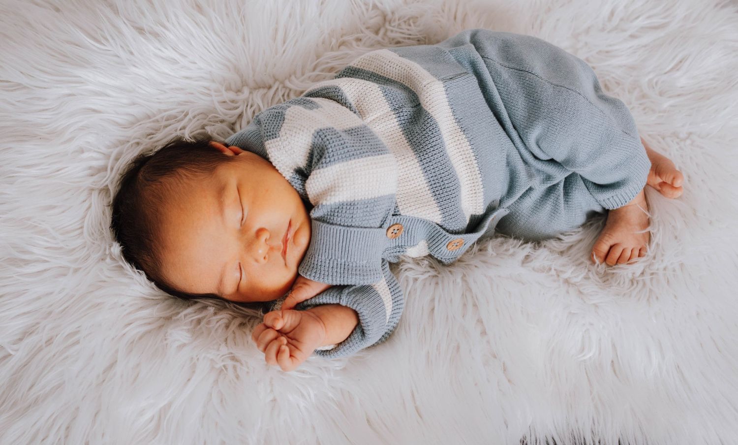 Sleeping newborn in cozy gray outfit resting peacefully on soft white fur blanket.