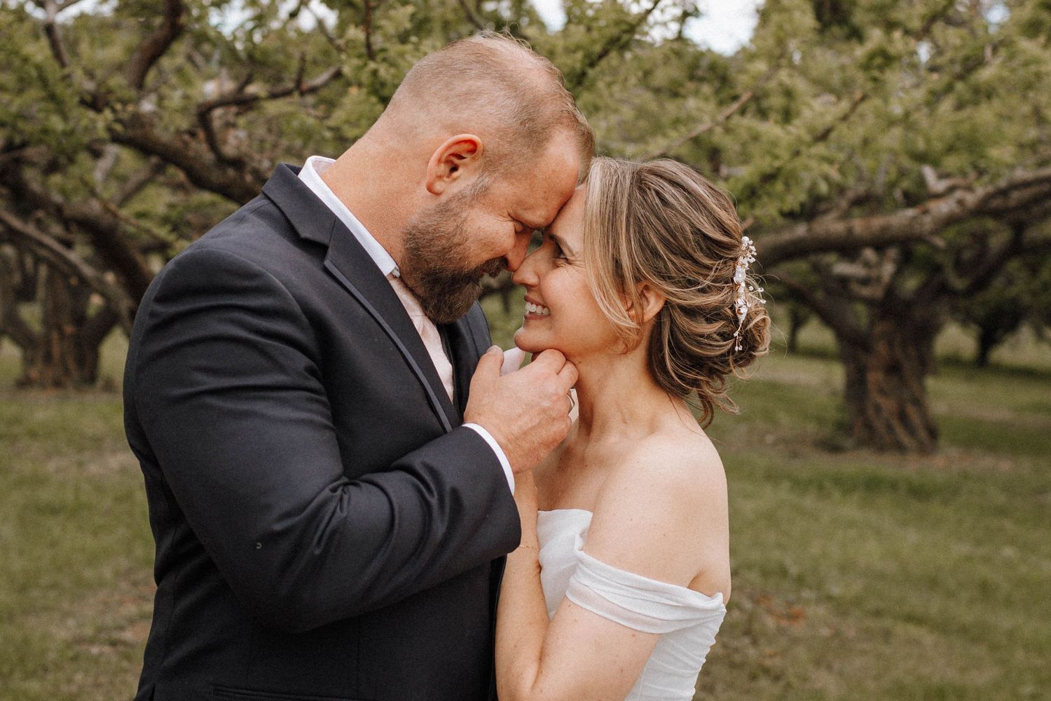 A romantic wedding portrait of a couple sharing an intimate moment in a blooming orchard garden.