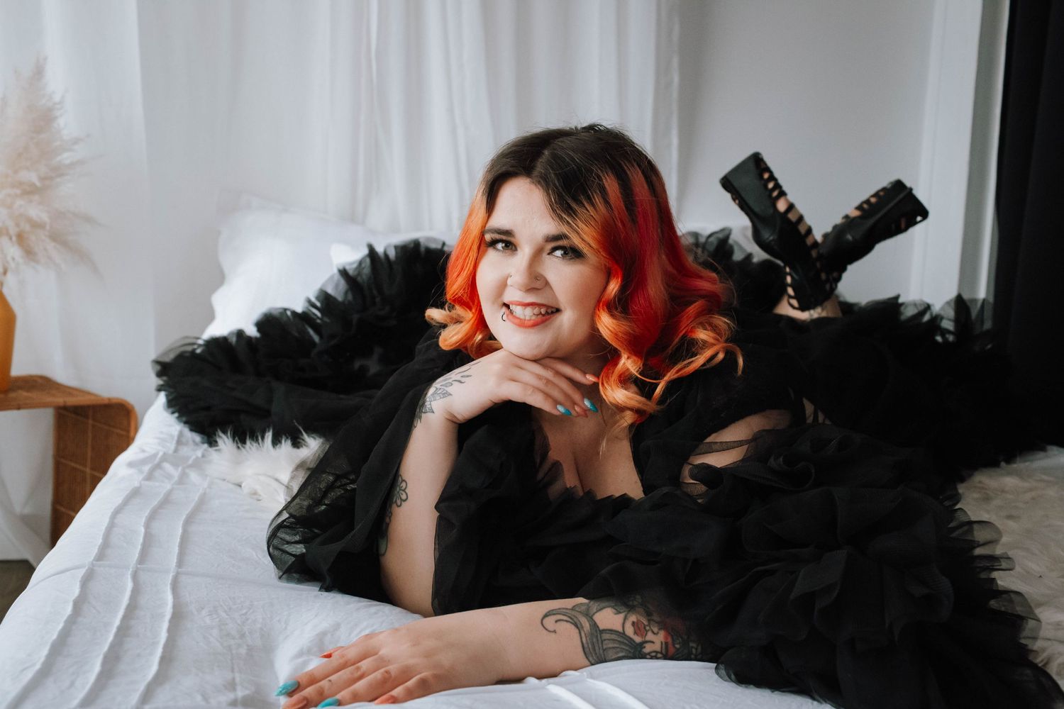 Glamour portrait on white bedding with black fur wrap and camera equipment.