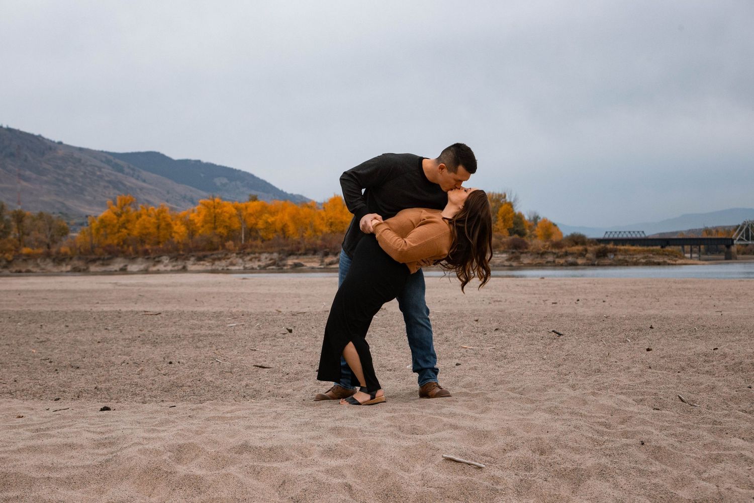 A romantic dip pose captured against autumn trees and mountains in the background.
