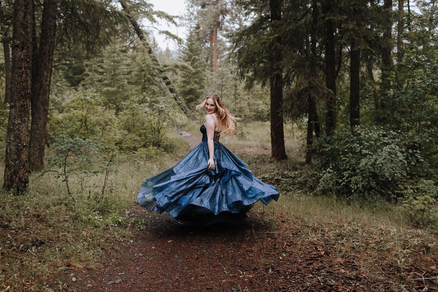 The skirt of a navy blue ballgown spins dramatically in a wooded forest setting.