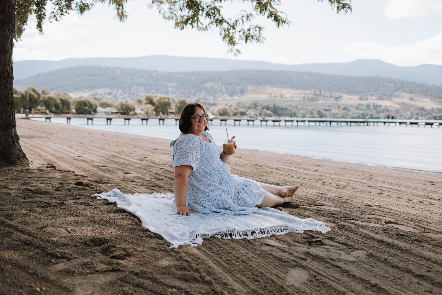 Scenic beach picnic setting with mountains and pier in background.