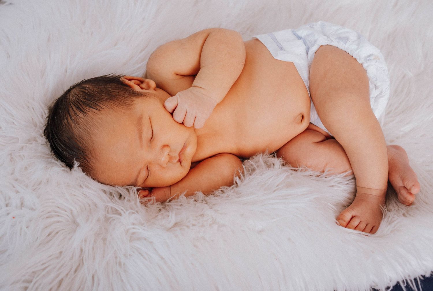 Sleeping baby on soft white furry rug in natural lighting.