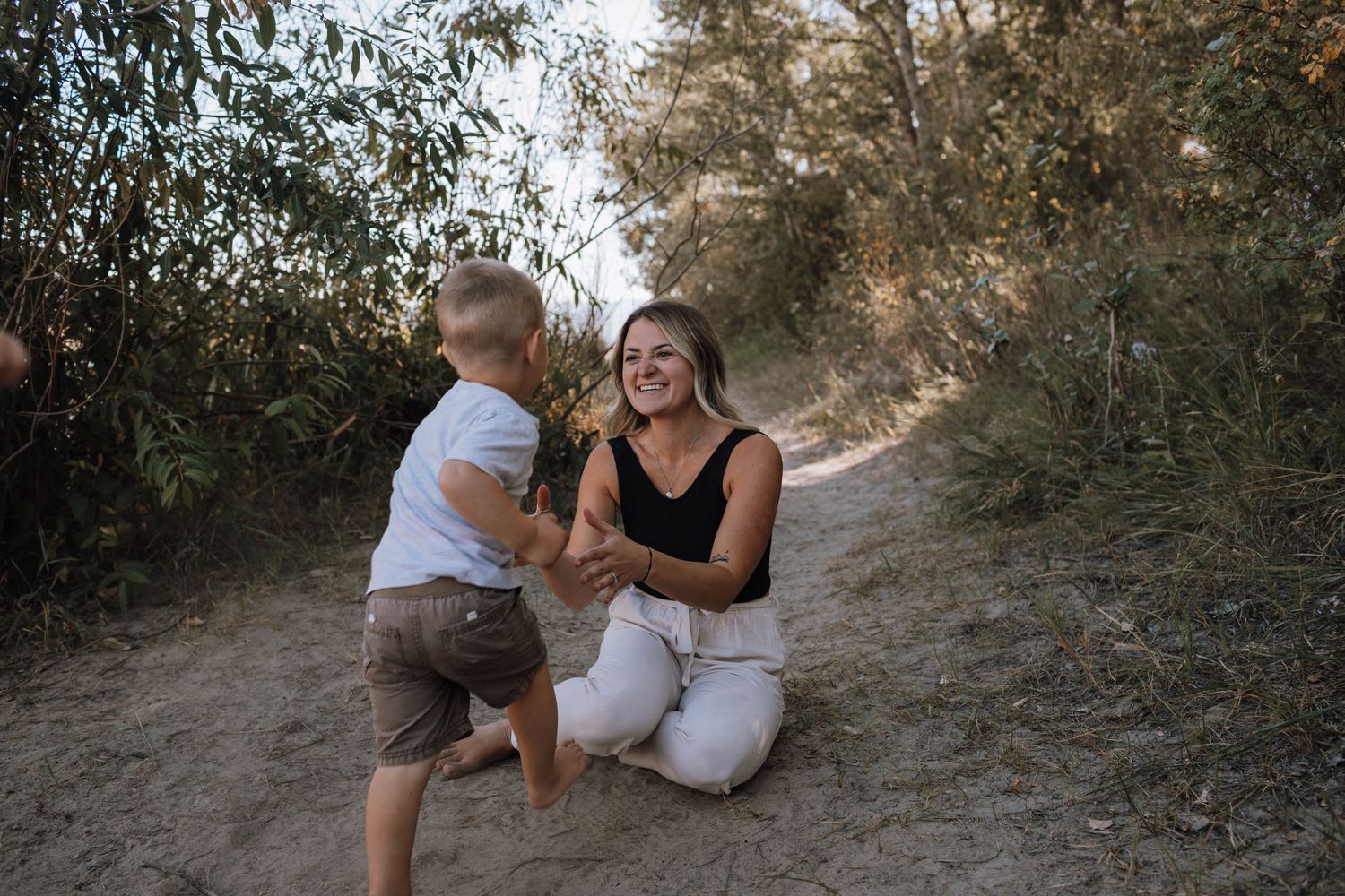 Two figures sharing a joyful moment on a sunlit dirt trail surrounded by greenery.