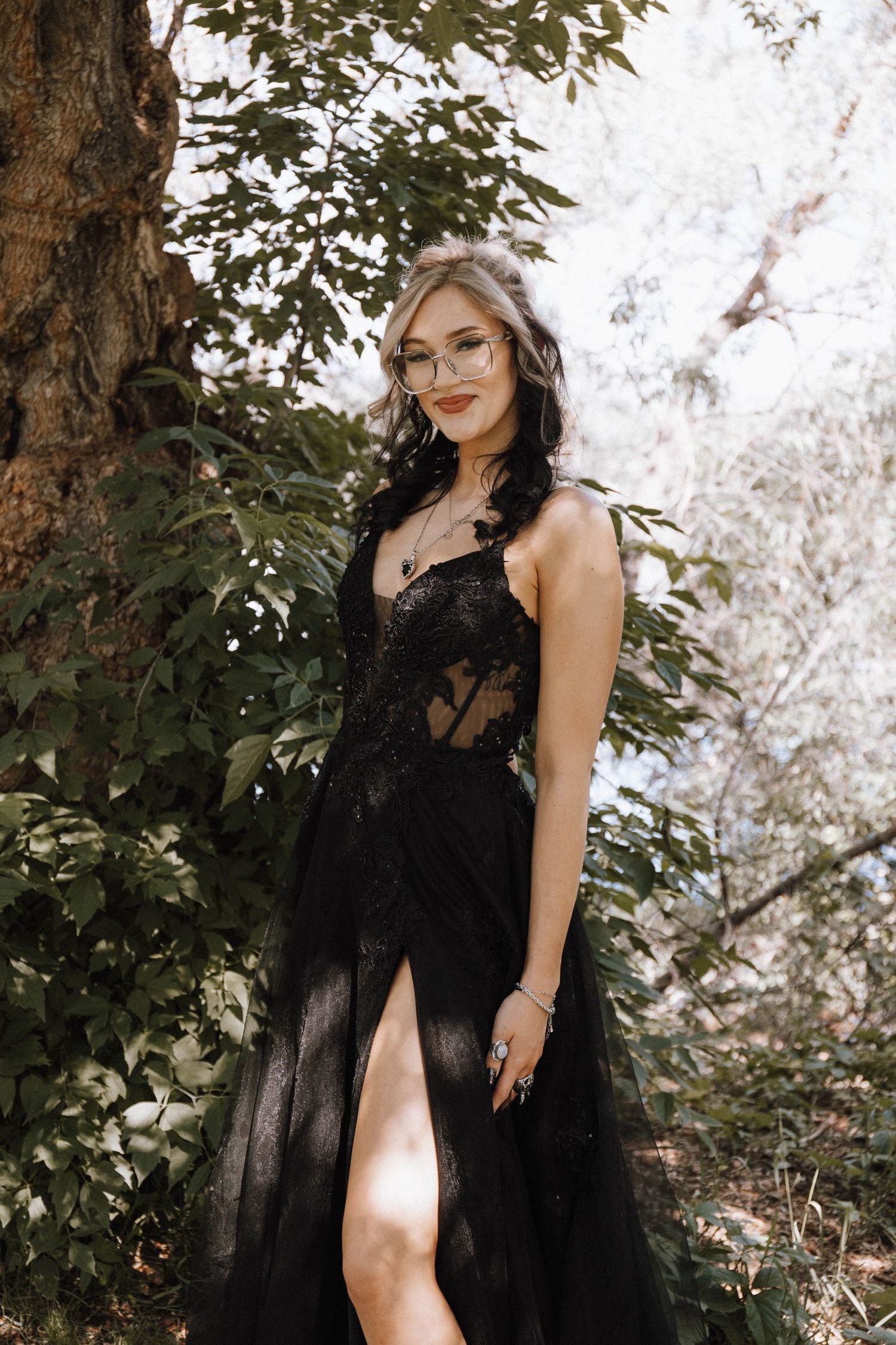 Artistic outdoor photoshoot featuring dramatic black tulle dress among green foliage in natural lighting.