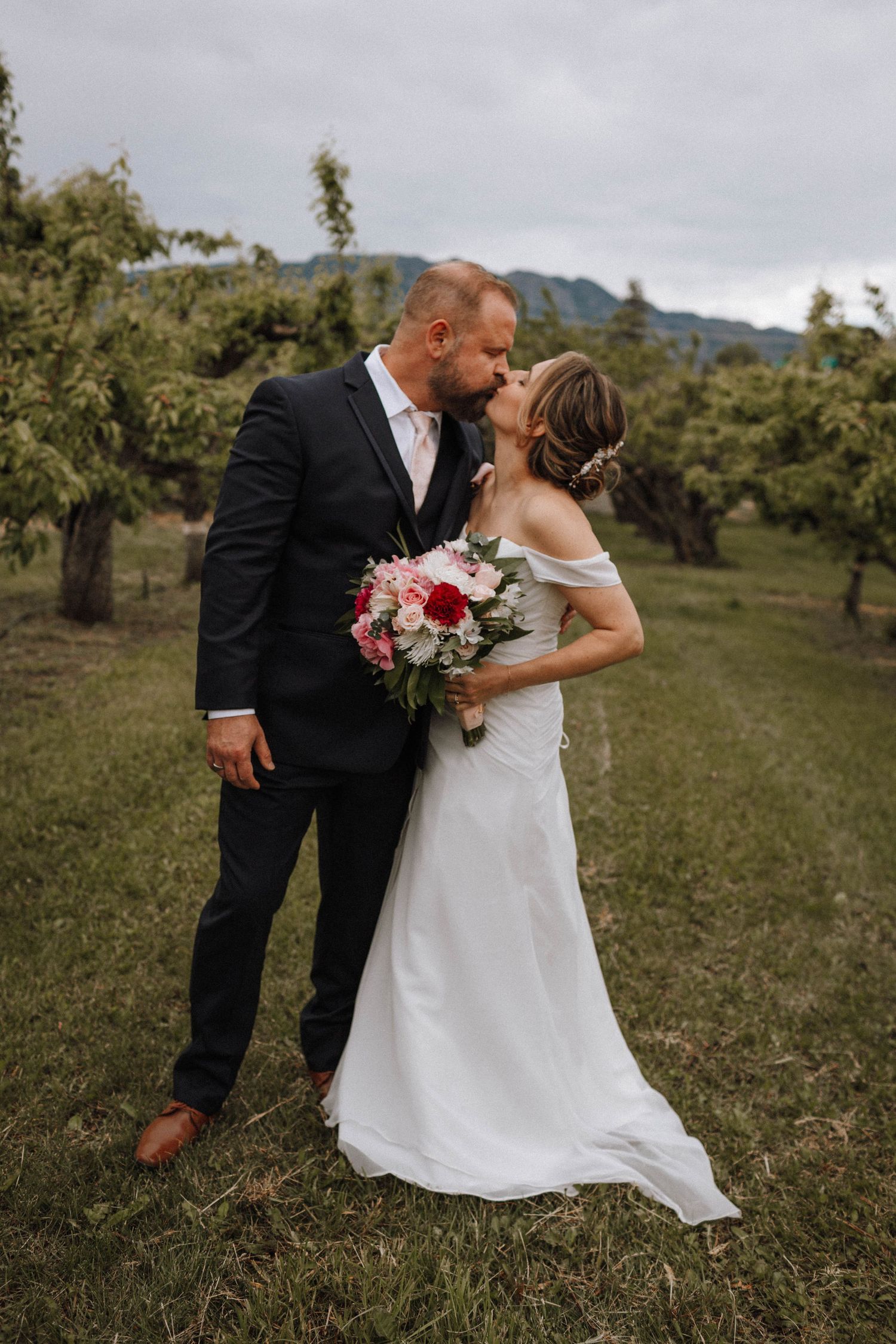 Wedding couple shares intimate moment in scenic mountain orchard.