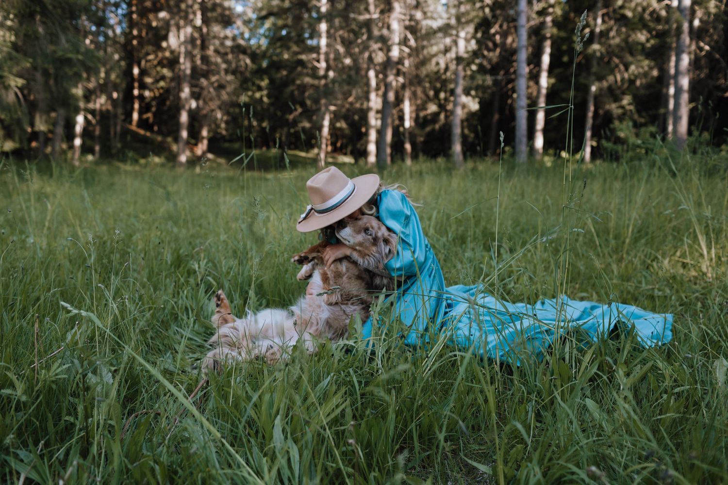 Person in turquoise dress relaxes in tall grass with furry companion.