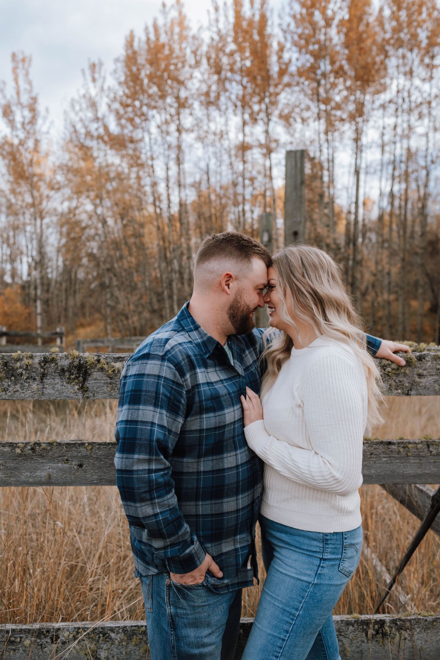 Romantic couple moment by rustic fence with fall foliage in background.