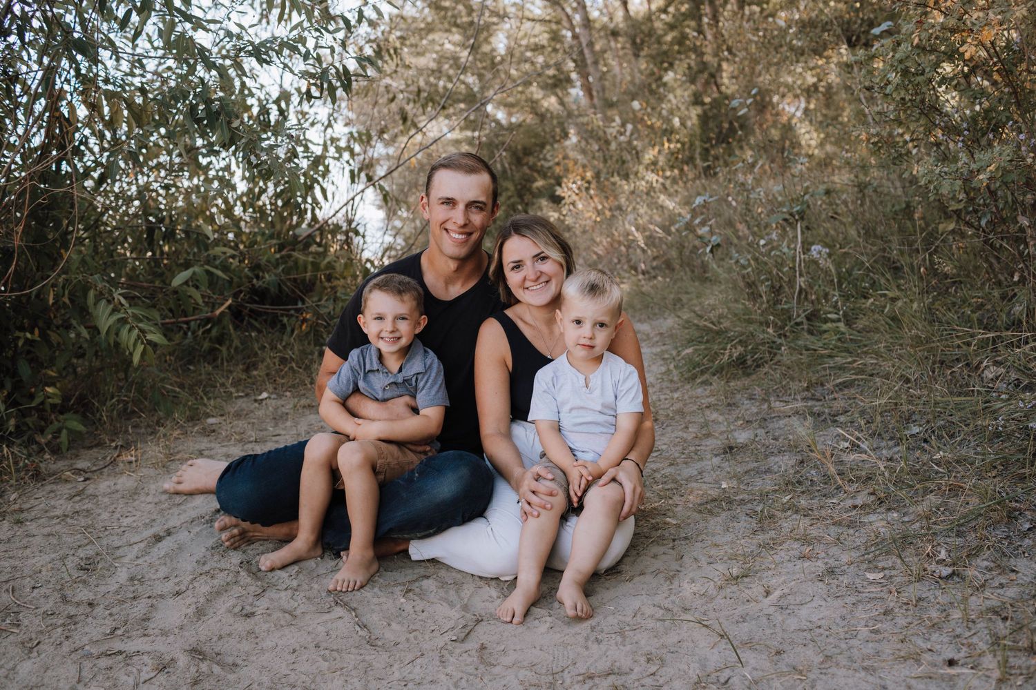 An outdoor family portrait on a dirt path with natural greenery in the background.