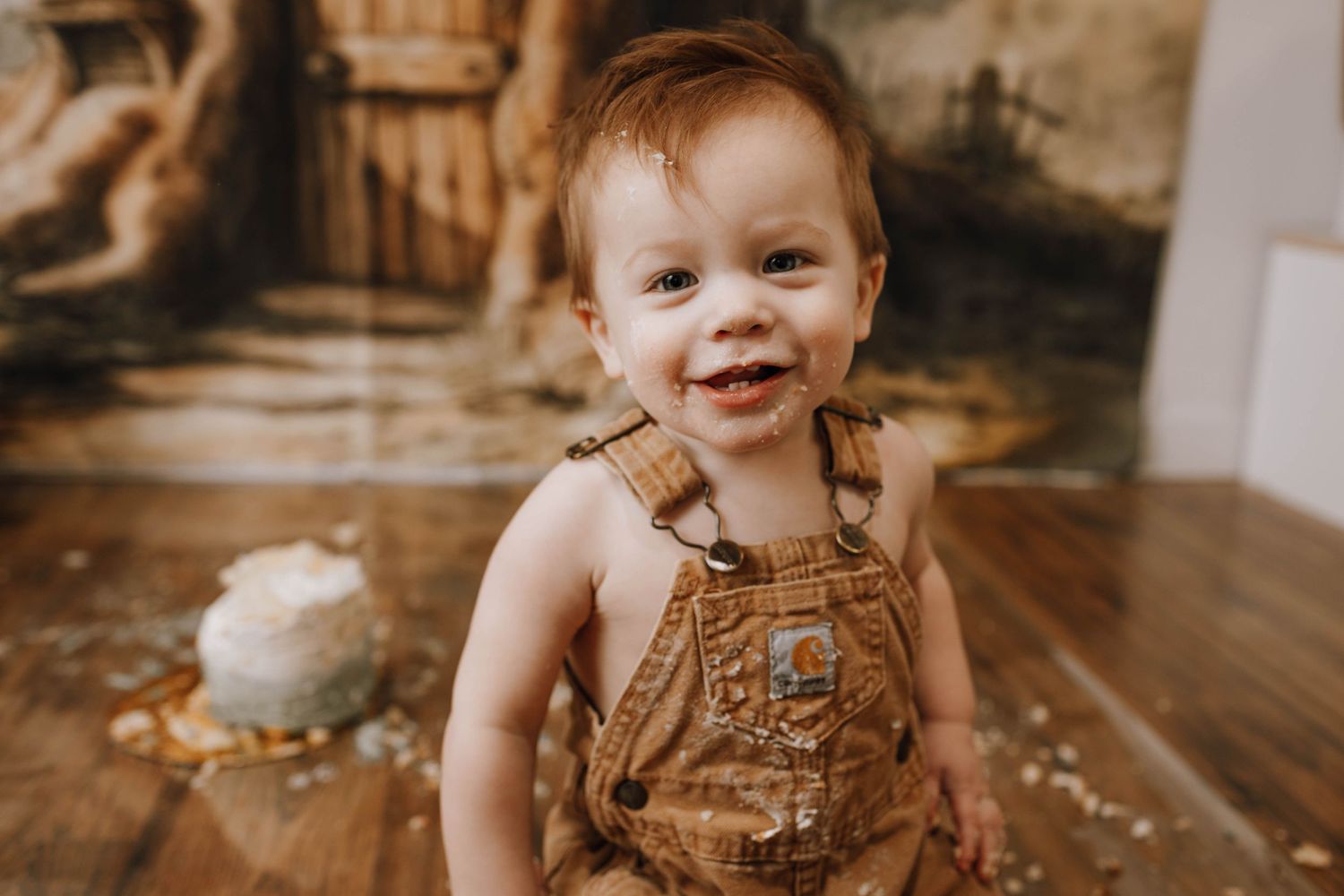 Toddler in brown overalls smiling and playing with baking ingredients.