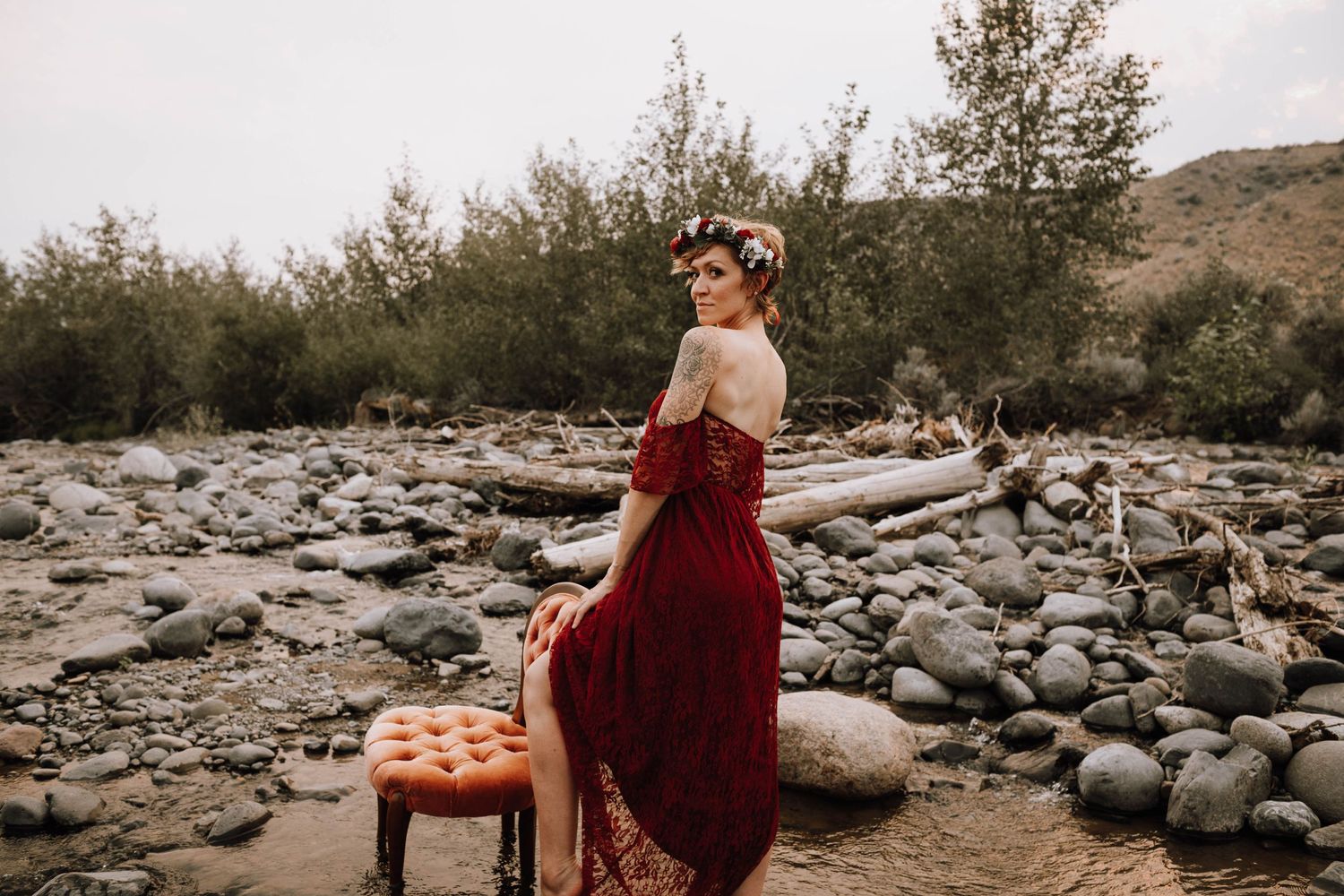 A romantic photoshoot with a burgundy dress on a rocky riverbed with vintage chair prop.