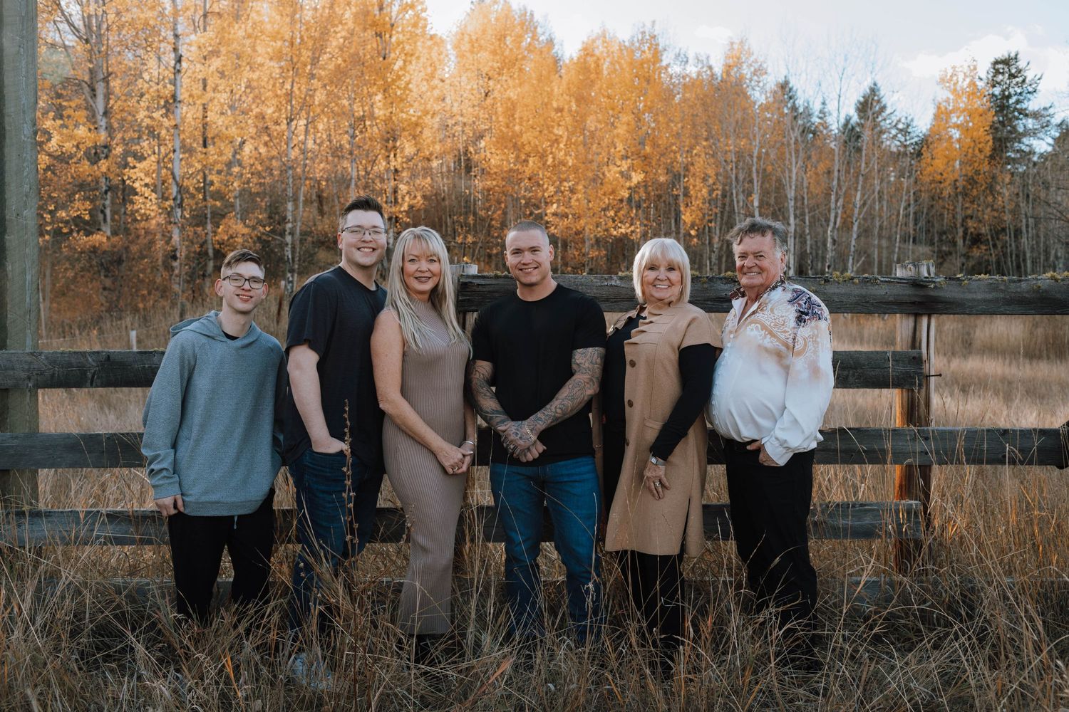 A group poses together in front of a wooden fence with autumn trees in the background.