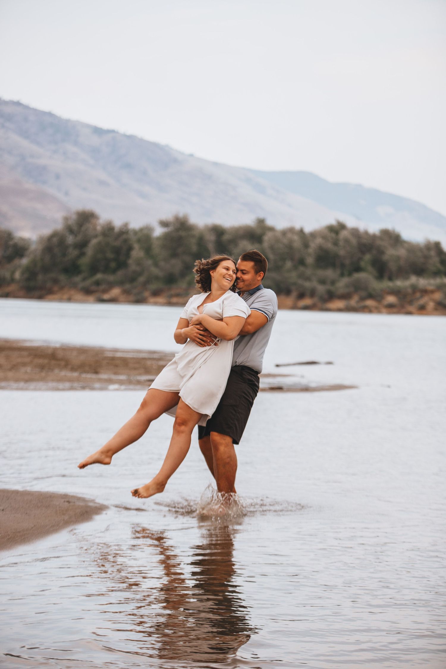 A playful couple enjoys a moment in the water with mountains visible in the distance.