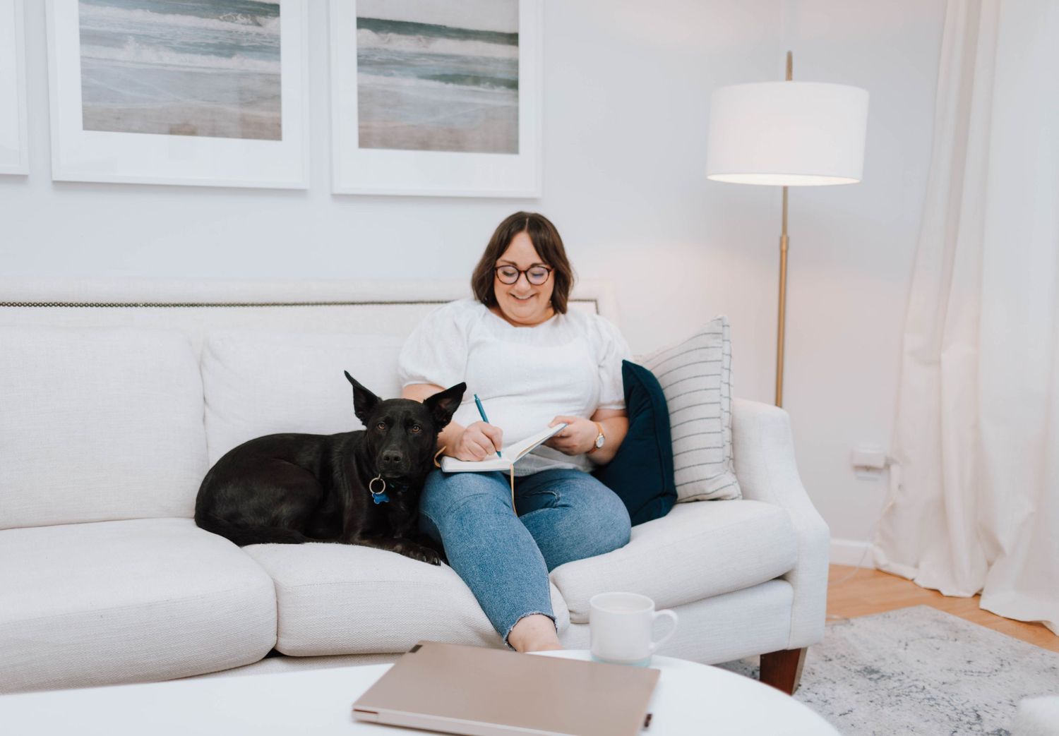 A living room setting with someone sitting on a white couch alongside a black cat.